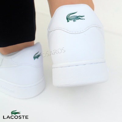 Calcanhares de ténis brancos Lacoste com logo verde, usados por pessoa com calças pretas