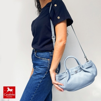 Mulher com bolsa azul clara de pele ao ombro, t-shirt azul e jeans