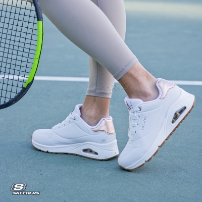 Ténis brancos Skechers com detalhes em rosa claro num campo de ténis junto a uma raquete preta e verde