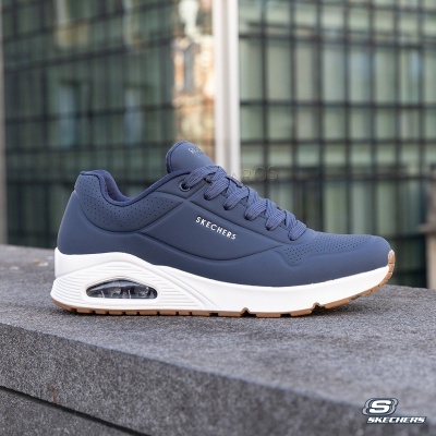 Ténis Skechers azul escuro com sola branca e castanha colocados numa superfície de pedra cinzenta