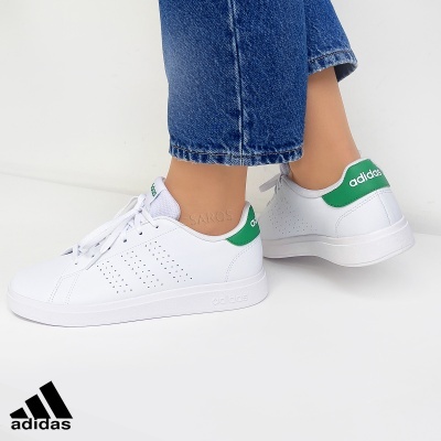Sapatilhas Adidas brancas com detalhes verdes usadas com calças de ganga