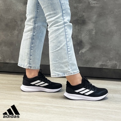 Ténis Adidas pretos com riscas brancas usados com calças de ganga