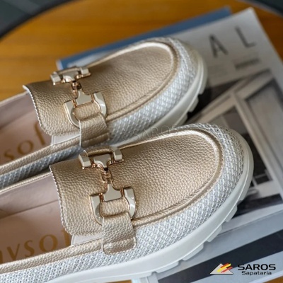Sapatos mocassim dourados com detalhes metalizados e laterais em malha branca sobre mesa de madeira.