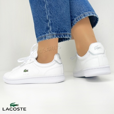 Sapatilhas brancas Lacoste com logotipo crocodilo e jeans azuis