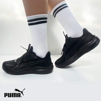 Sapatilhas desportivas negras Puma com meias brancas riscas negras num fundo branco.