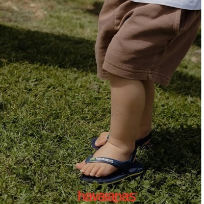 Criança com sandálias havaianas azuis e tiras verdes e pretas em relva