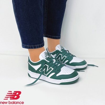 Ténis New Balance verdes e brancos com sola branca usados com calças de ganga azul escuro