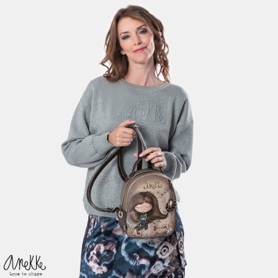 Mala pequena castanha com ilustração de menina, usada por mulher com camisola cinza e saia floral.