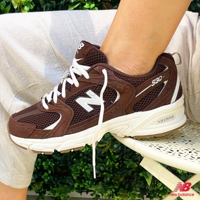 Ténis New Balance 530 castanhos com detalhes brancos usados por pessoa sentada