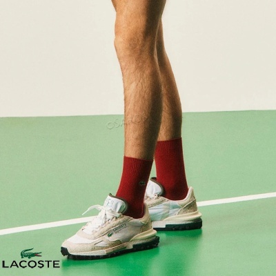 Ténis Lacoste bege e branco usados com meias vermelhas em piso verde claro