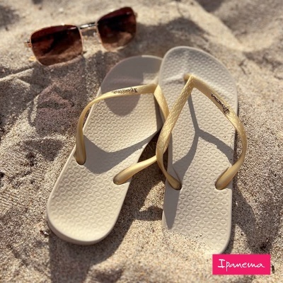 Chinelos bege em areia com óculos de sol castanhos e logo Ipanema