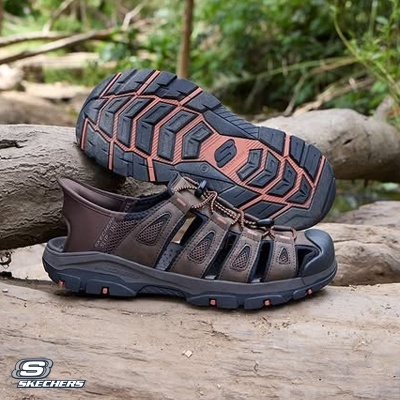 Sandálias Skechers castanhas com sola robusta preta e castanha numa superfície de madeira