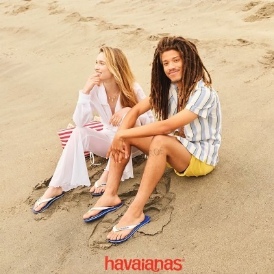 Casal jovem na praia usando chinelos Havaianas, logótipo havaianas em vermelho no fundo