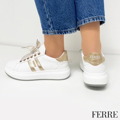 Sapatilhas brancas com detalhes dourados e a marca FERRE, usadas com calças de ganga.