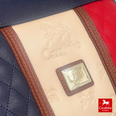 Detalhe de mala com couro e tecido azul, vermelho e bege com emblema Cavalinho