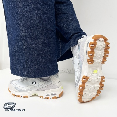 Sapatilhas Skechers brancas com sola castanha e calças de ganga azul.