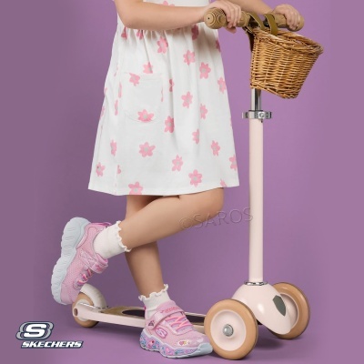 Criança em trotinete beje com cesto de vime, vestindo vestido branco com flores cor de rosa, meias brancas e ténis rosas Skechers