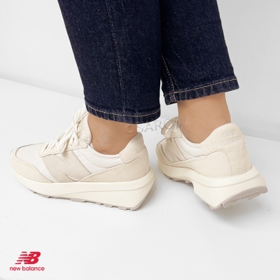 Ténis New Balance bege claro vistos de costas e lateral, com sola branca.