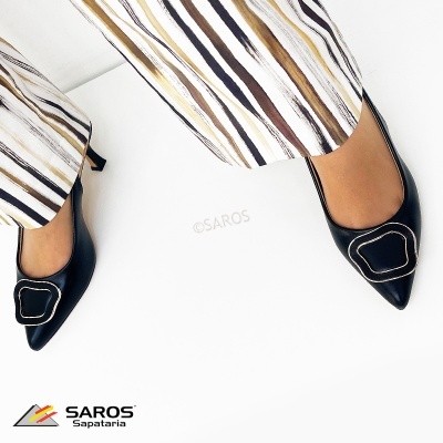 Sapatos de salto alto pretos com adorno metálico e calças riscas castanhas e pretas
