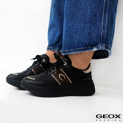 Ténis negros Geox com detalhes dourados e bege usados com calças de ganga azuis