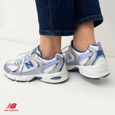 Ténis New Balance 639 branco, azul e prateado em pessoa com calças de ganga azuis.