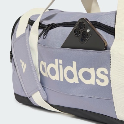 Mala de desporto lilás com alças brancas e o texto adidas na lateral e um telemóvel preto no bolso frontal.