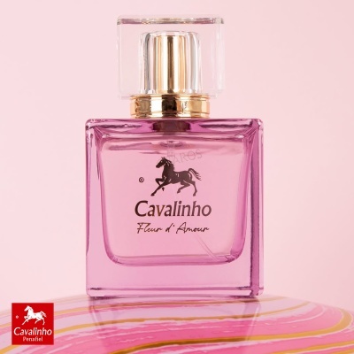 Frasco de perfume rosa Cavalinho Fleur dAmour sobre superfície rosa e amarela.