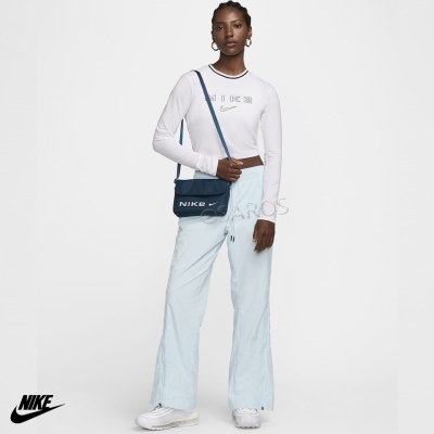 Mulher vestindo top branco Nike, calças azuis claras largas, ténis brancos e mala Nike azul escura ao ombro