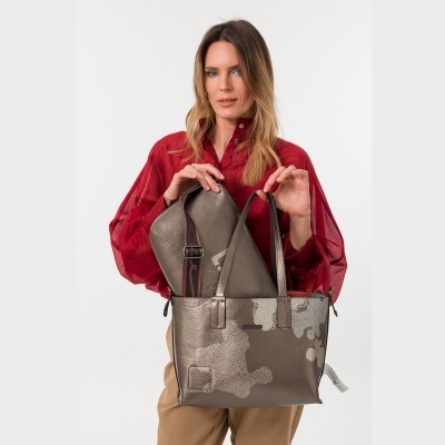 Bolsa metálica bronze com padrão abstrato nas mãos de mulher com camisa vermelha e calças bege