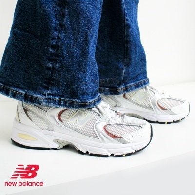 Sapatilhas New Balance brancas com detalhes cinza e castanho usadas com calças de ganga azuis