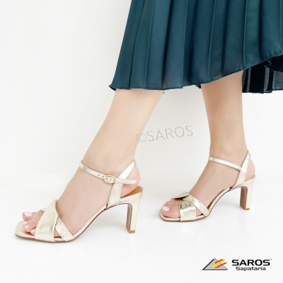 Sandálias douradas de salto médio com tiras cruzadas e fivela no tornozelo, pé feminino com saia azul