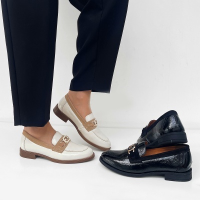 Dois pares de sapatos mocassim femininos, um branco com detalhes castanhos claros e fivela dourada, outro preto brilhante com detalhe em camurça.
