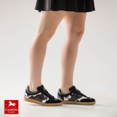 Tênis Cavalinho Penafiel preto e branco com sola caramelo usados por pessoa com saia preta