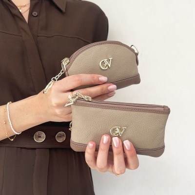 Duas carteiras pequenas de pele bege com logótipo CV em mãos femininas com camisa castanha e botões grandes.