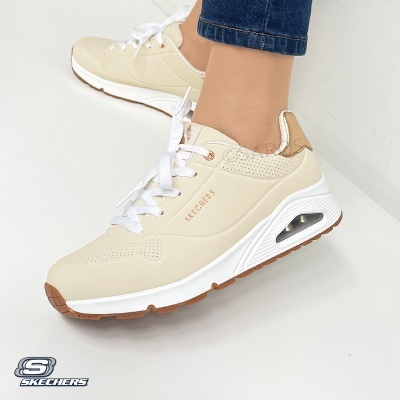 Ténis bege Skechers com sola branca e base castanha mostrados em fundo branco