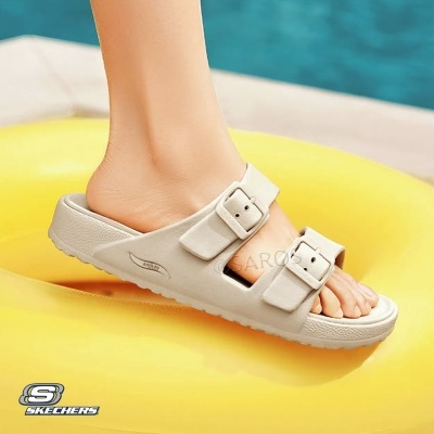 Chinelo Skechers bege claro com duas fivelas, pé numa bóia amarela junto a uma piscina
