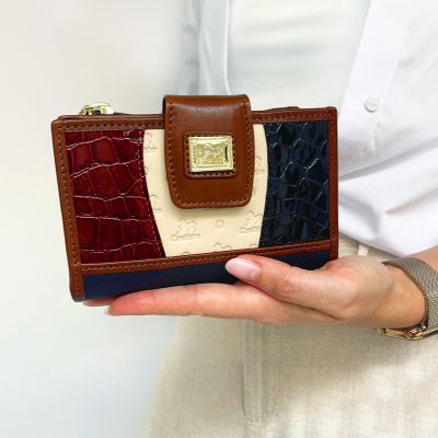 Carteira feminina em materiais variados com padrão crocodilo, detalhes em bege com relevo, fecho castanho com placa metálica, segurada por uma mão com camisa branca.
