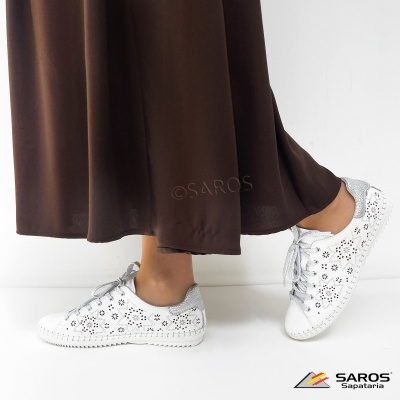 Ténis brancos com recortes florais e detalhes prateados num fundo branco.