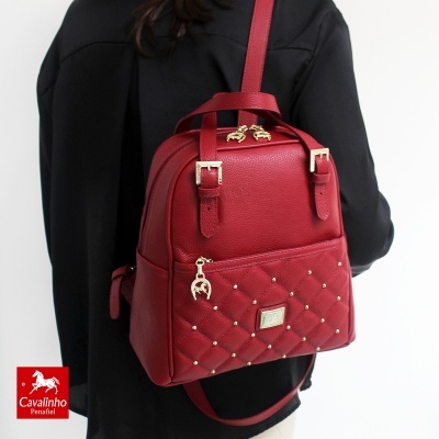 Mochila vermelha em couro sintético com tachas douradas e fechos metálicos dourados, usada por pessoa de camisa preta