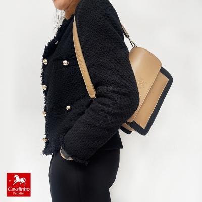 Mala de ombro Cavalinho bege e preta usada por pessoa de casaco preto.