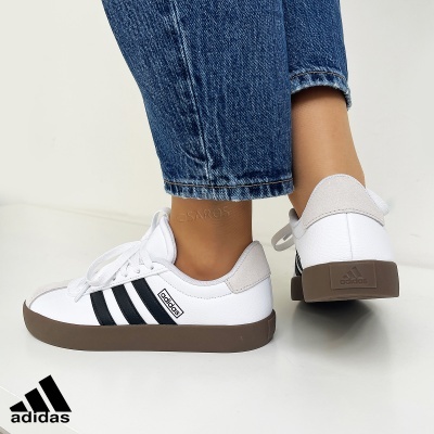 Ténis Adidas Campus brancos com riscas pretas e sola castanha usados com jeans azuis