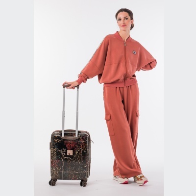 Mulher com fato de treino terracota e mala de viagem preta com padrão colorido