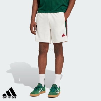 Homem a usar calções brancos Adidas com riscas laterais verdes e vermelhas, ténis verdes e meias brancas