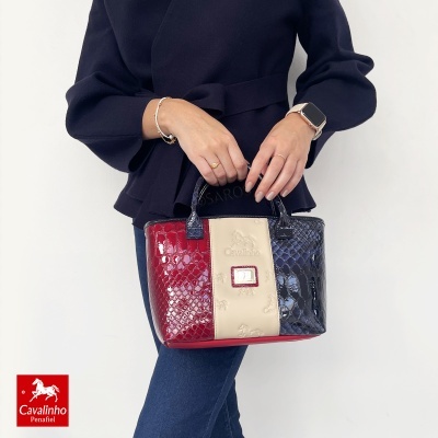 Mala de mão em verniz tricolor com padrão de pele, logo Cavalinho, mãos femininas com pulseira e relógio