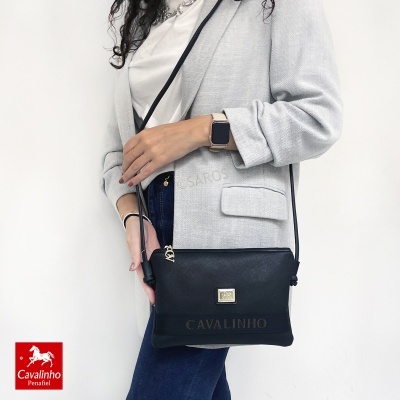 Mala de ombro preta Cavalinho usada por mulher com blazer cinza e jeans azul