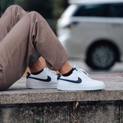 Ténis desportivos Nike brancos com detalhes azul escuro usados com calças castanhas claras