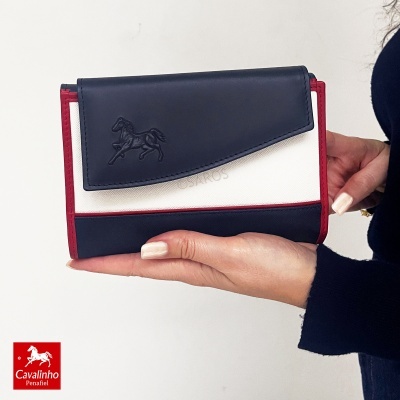 Carteira feminina azul, branca e vermelha com relevo de cavalo e a palavra CAVALINHO, segurada numa mão num fundo claro