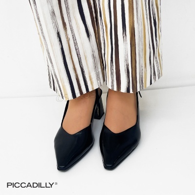 Sapatos pretos de salto quadrado com bico fino em verniz e calças com riscas verticais em fundo branco.