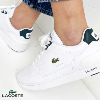 Ténis Lacoste brancos com detalhes verdes e logo crocodilo, usados com calças de ganga azuis