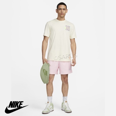 Homem com roupa desportiva creme e rosa, segurando saco verde com logo Nike